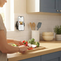 A magnetic phone holder attached to kitchen tiles holding a smartphone displaying a recipe